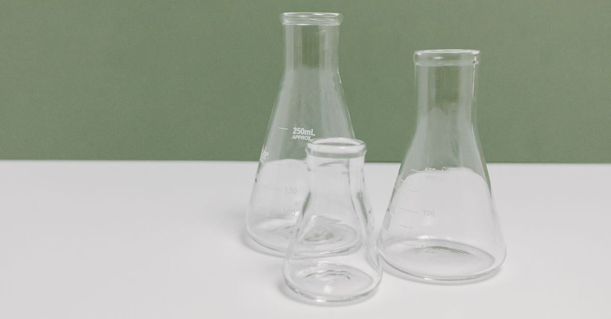 A set of three clear glass laboratory flasks on a clean white and green background, ideal for science themes.